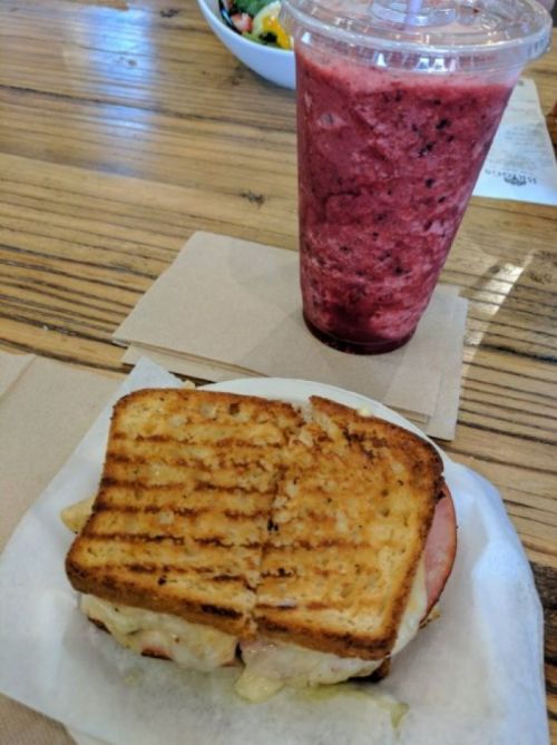 A grilled sandwich with melted cheese and ham, served with a berry smoothie on a wooden table.