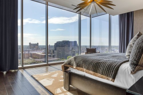 Modern bedroom with a large window showcasing a city view, featuring a stylish bed and decorative ceiling fan.