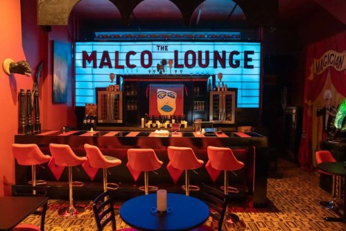 A vibrant bar scene at Malco Lounge, featuring colorful decor, a striking mural, and stylish seating.