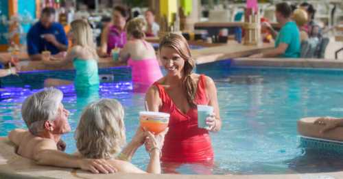 A woman in a red swimsuit serves drinks to two people in a pool, with others enjoying the vibrant atmosphere around them.