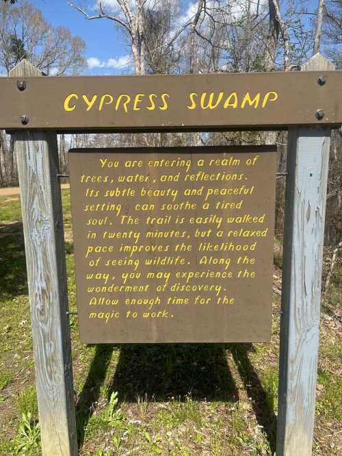 Sign at Cypress Swamp entrance, describing the tranquil trail and wildlife experience in a serene natural setting.