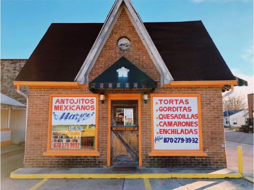 A brick building with a peaked roof, featuring signs for a Mexican restaurant offering various dishes and contact information.