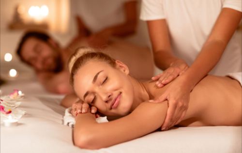 A woman enjoys a relaxing massage in a serene spa setting, with a man receiving a massage in the background.