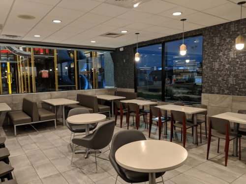 Interior of a fast-food restaurant with tables, chairs, and large windows showing a playground outside.
