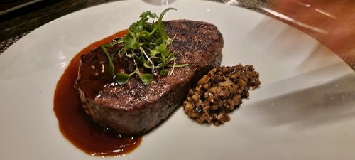 A perfectly cooked steak on a white plate, garnished with herbs and accompanied by a side of finely chopped mushrooms.