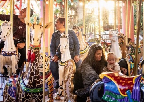 A carousel with colorful animal figures, featuring adults and a child enjoying a ride together.