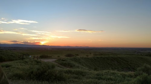 A serene sunset over rolling hills, with vibrant orange and purple hues in the sky and distant mountains on the horizon.