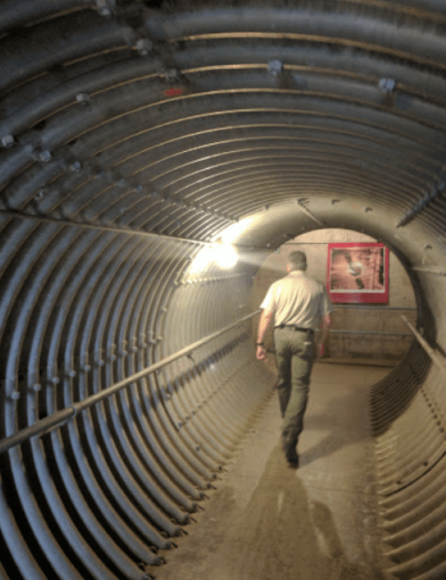 A person walks through a dimly lit, curved metal tunnel with ribbed walls.