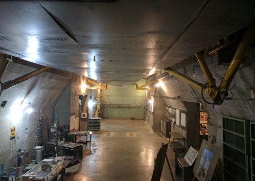Interior of a dimly lit underground facility with concrete walls, yellow support beams, and various equipment.