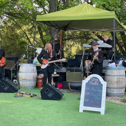 A band performs outdoors under a canopy, with instruments and amplifiers set up near wooden barrels.