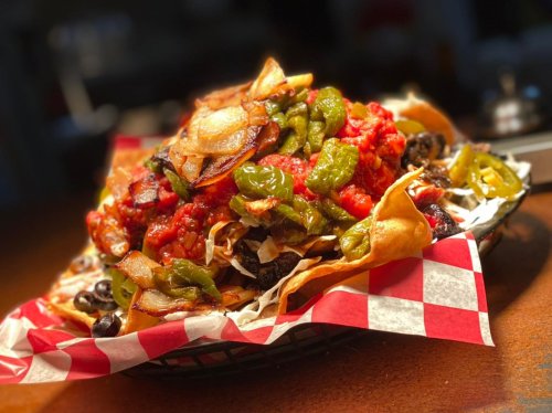 A colorful plate of nachos topped with salsa, jalapeños, black olives, and crispy onions on a checkered paper.