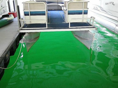 A boat docked over bright green water, with a clear view of the boat's underside and the dock.
