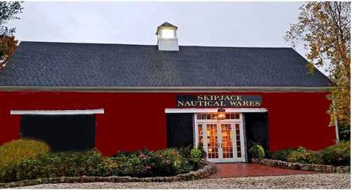 A red building with a sloped roof and a sign reading "Skipjack Nautical Wares," surrounded by greenery and a brick path.