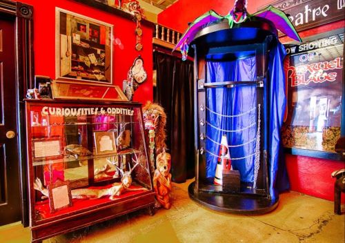 A vibrant room featuring a display case of curiosities and an ornate stage with colorful drapes and props.