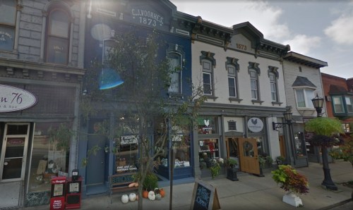 Historic storefronts line a street, featuring a blue building with "C.J. Johring 1873" and various shops.