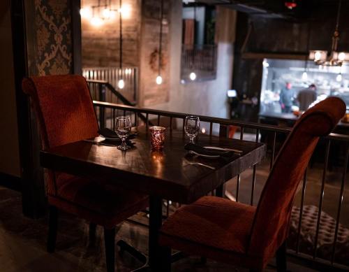 Cozy restaurant setting with a wooden table, two chairs, and candlelight, featuring a stylish industrial backdrop.