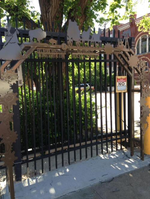 A decorative metal gate with intricate designs, featuring wagon motifs and a "No Trespassing" sign.