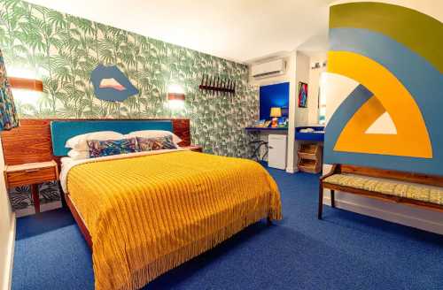 A colorful hotel room featuring a yellow bedspread, tropical wallpaper, and modern decor.