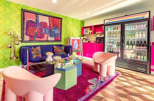 A vibrant living space featuring colorful furniture, a patterned rug, and a fridge stocked with drinks against a bold backdrop.