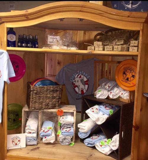 A wooden display shelf filled with T-shirts, towels, and colorful plates, showcasing a beach-themed merchandise collection.