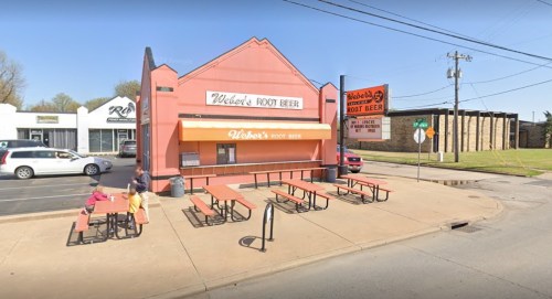 A pink building with "Weber's Root Beer" signage, featuring outdoor seating and a nearby parking area.