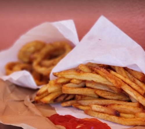 A pile of golden French fries with a side of ketchup, next to a serving of onion rings in paper containers.