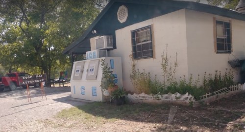 A small building with "ICE" signs outside, featuring an air conditioning unit and a sign for an attendant.