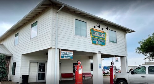 Exterior of a two-story building with a sign reading "Luvville Roadhouse" and vintage gas pumps in front.