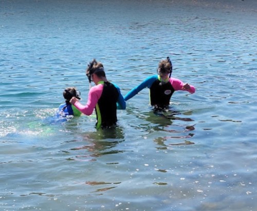 Three children in colorful swimsuits play in shallow water, enjoying a sunny day at the beach.