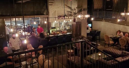 A cozy restaurant interior with diners at tables, a bar area, and warm lighting creating an inviting atmosphere.