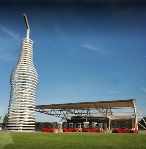 A unique gas station featuring a large, spiraled soda bottle structure and several red cars parked in front.