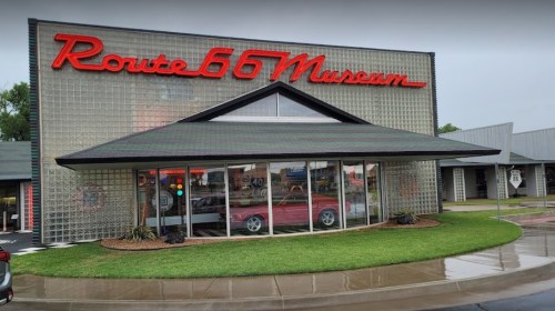 Exterior of the Route 66 Museum featuring a glass facade and a red vintage car visible through the entrance.