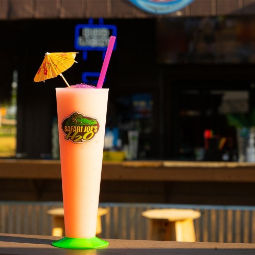 A colorful drink with a small umbrella and straw, set against a blurred bar background.
