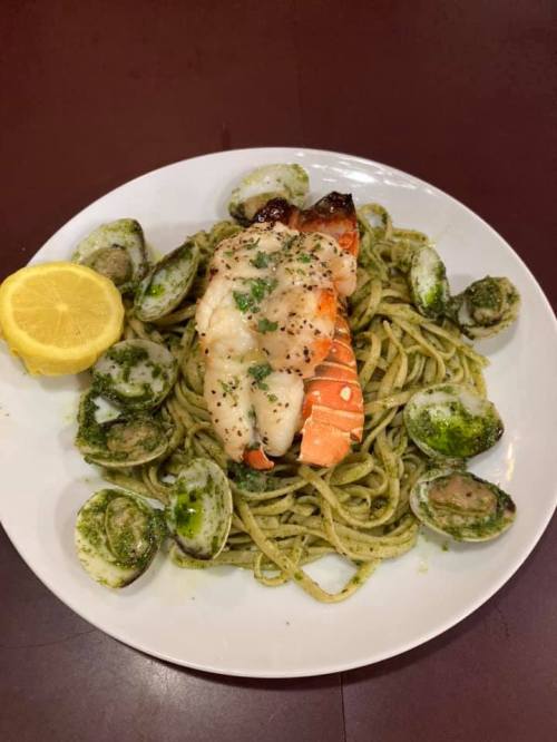 A plate of pasta topped with shrimp and clams, served with a lemon wedge and pesto sauce.