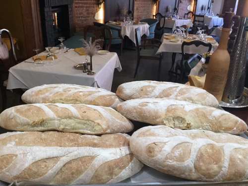 A tray of freshly baked bread loaves on a table in a cozy restaurant setting.