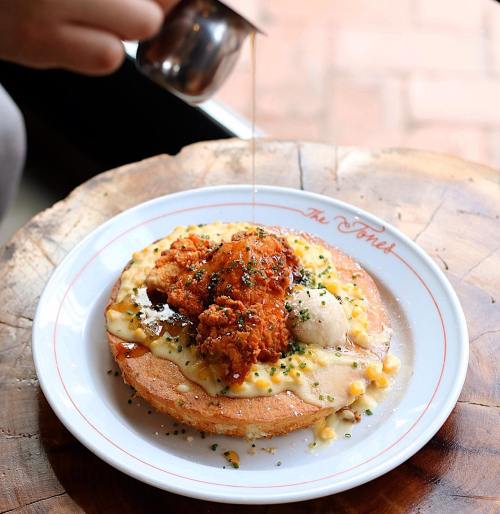 A plate of fried chicken on a biscuit with gravy, corn, and a drizzle of syrup, served on a wooden table.