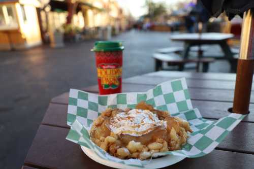 A plate of funnel cake topped with syrup sits on a table, with a festive drink in the background.