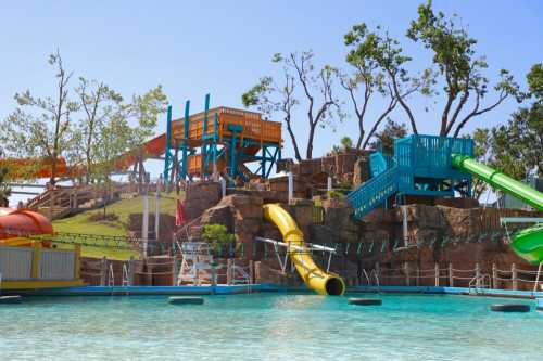 Colorful water slides and a play structure at a water park, surrounded by trees and a clear blue sky.