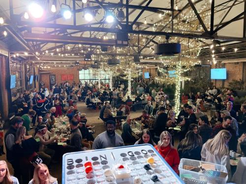 A lively indoor event with a large crowd seated at tables, decorated with string lights and festive decor.