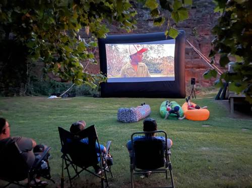 Outdoor movie night with people sitting on chairs, watching a film on a large inflatable screen in a grassy area.