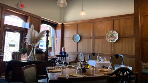 A cozy restaurant interior with wooden walls, elegant tables set for dining, and decorative plates on the wall.