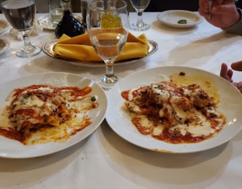Two plates of lasagna topped with marinara sauce and melted cheese, accompanied by a glass of water on a dining table.