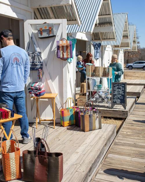 A vibrant outdoor market scene with colorful bags for sale and shoppers browsing at various stalls.