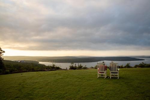 Two white chairs facing a serene lake view under a cloudy sky, surrounded by lush green grass.