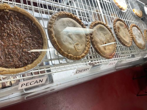 A display case with various pies labeled pecan, cherry, peach, and others, showcasing their golden crusts.