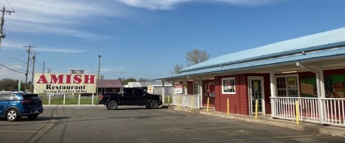 Exterior of an Amish restaurant with a large sign, featuring a parking lot and blue sky in the background.