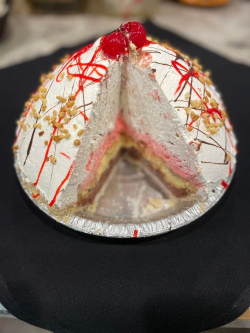 A dome-shaped cake with whipped cream, cherries, and nuts, partially sliced to reveal layers of pink filling and cake.