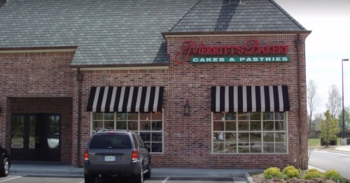 Exterior of Merritt's Bakery, featuring a brick facade, striped awnings, and a parked car in front.