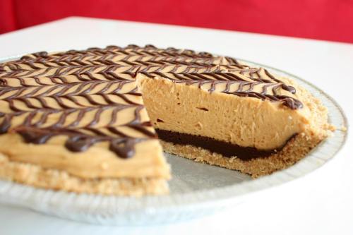 A creamy peanut butter pie with a chocolate layer and decorative chocolate drizzle, partially sliced on a silver pie dish.