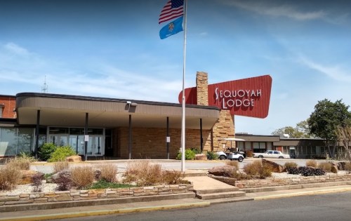 Exterior view of Sequoyah Lodge with a stone facade, American flag, and landscaped entrance.